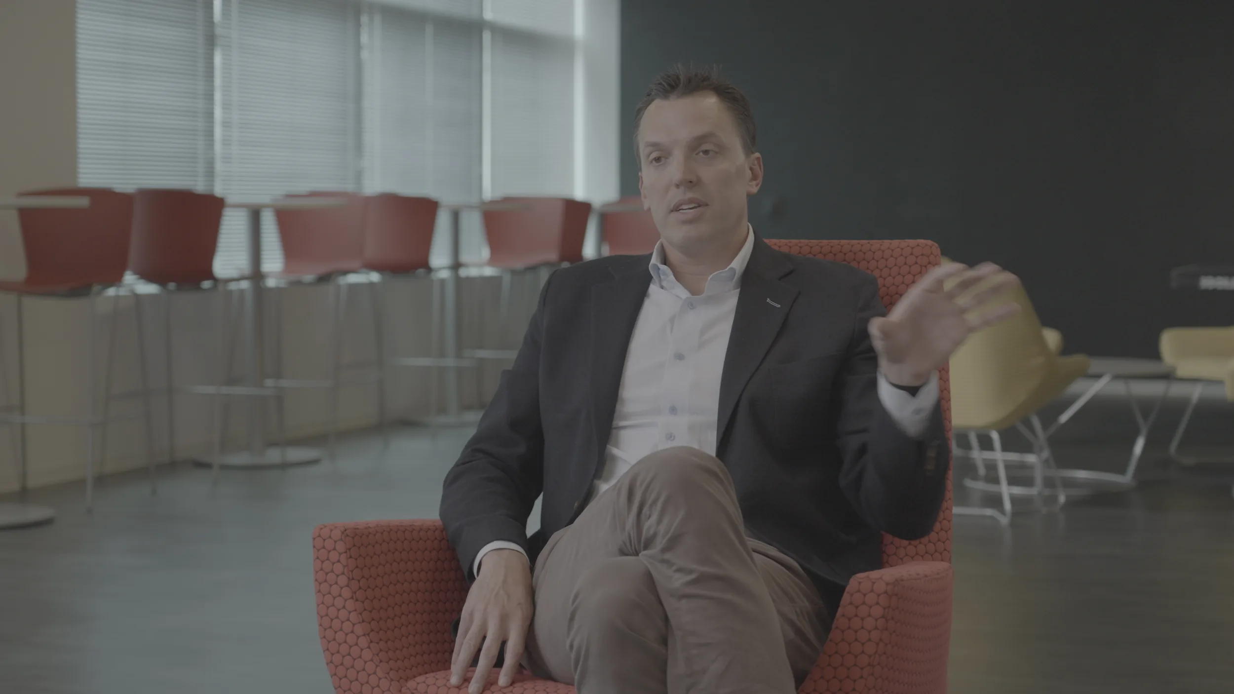 The A camera's flat S-Log3 original of a man in a navy blazer speaking from a red chair