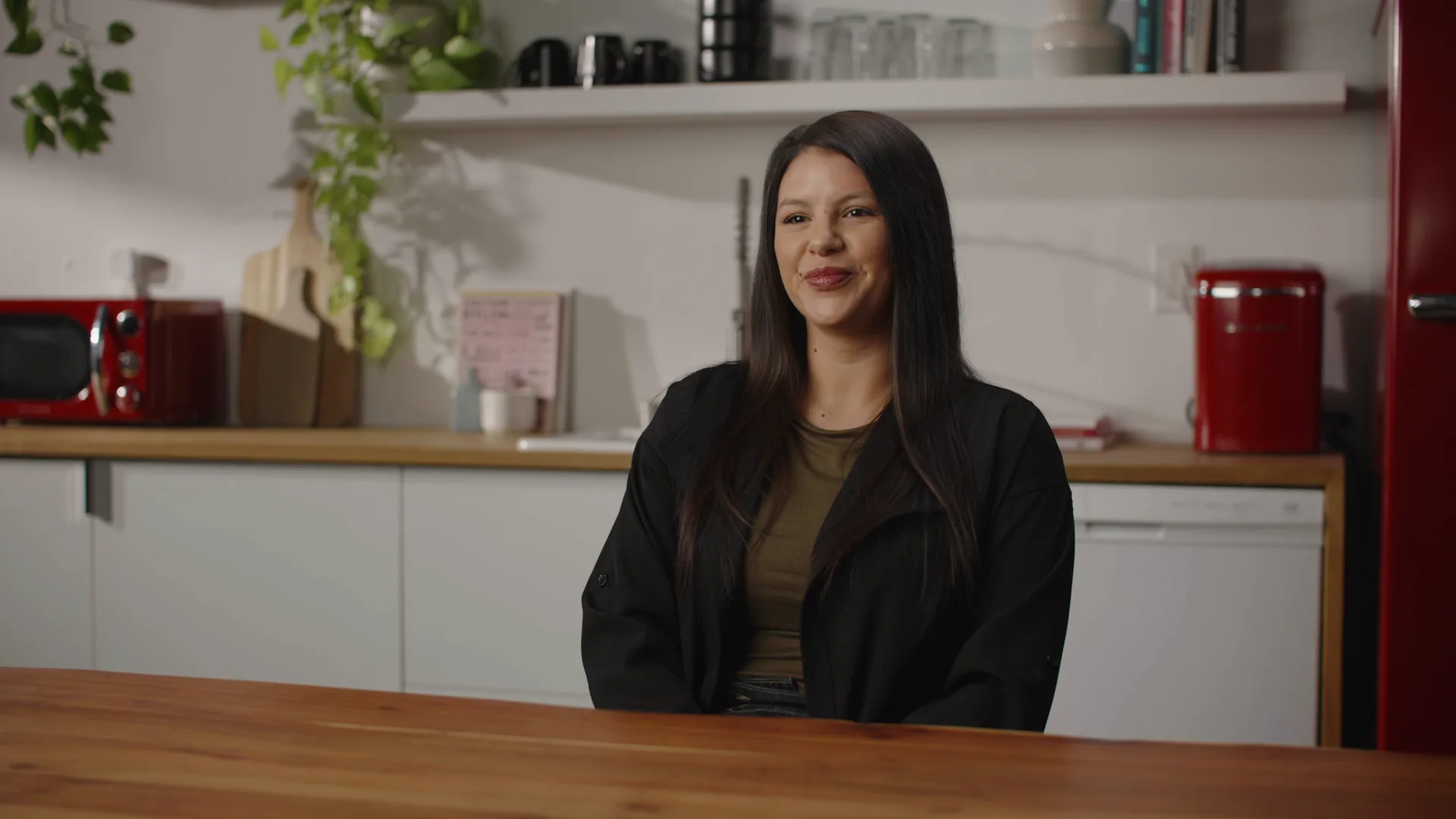 A camera production frame: the interview subject at the wood table in the kitchen set