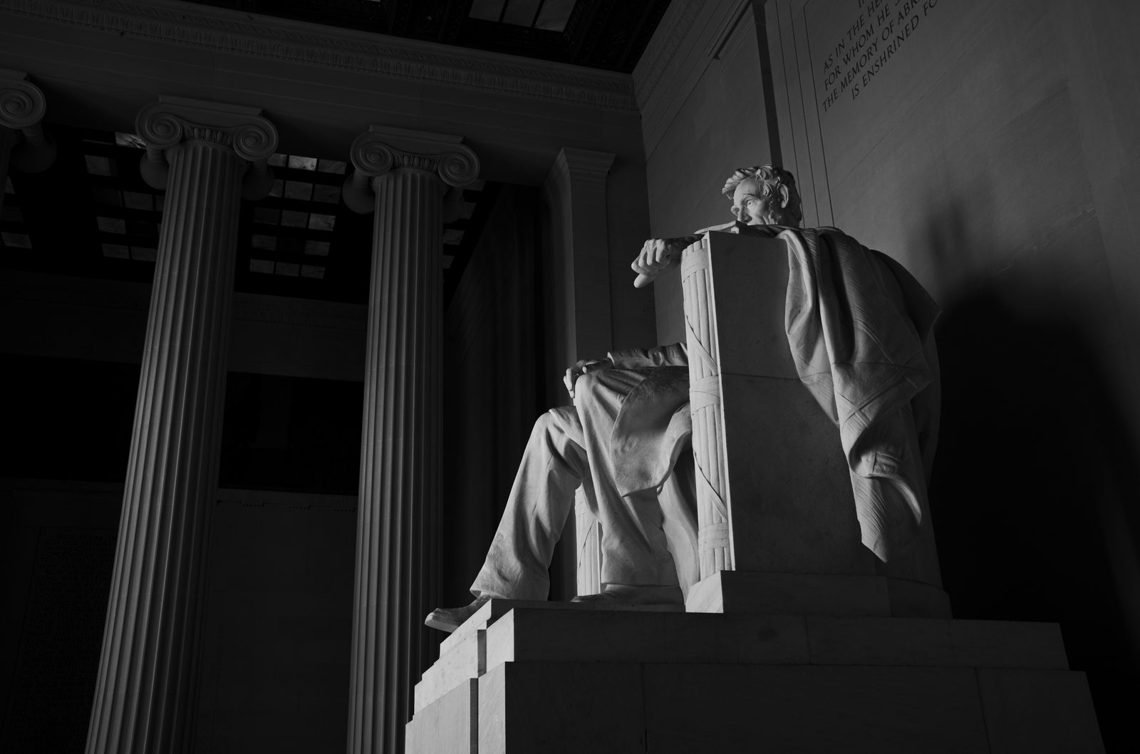 Black and white photo of the seated Lincoln statue in hard side light between tall columns.