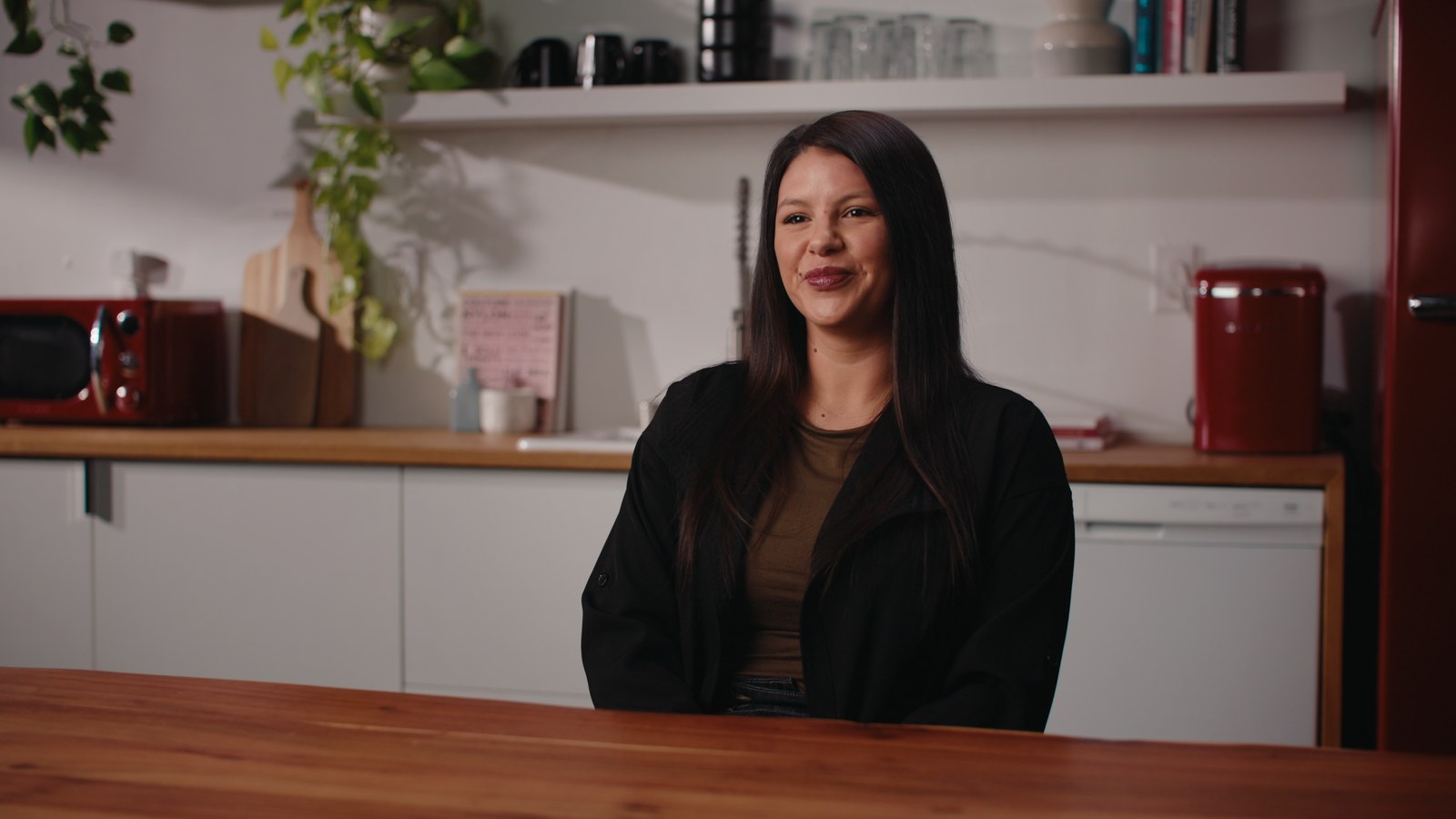 The same interview setup on the shoot day, graded: a woman at a kitchen table in soft side light.