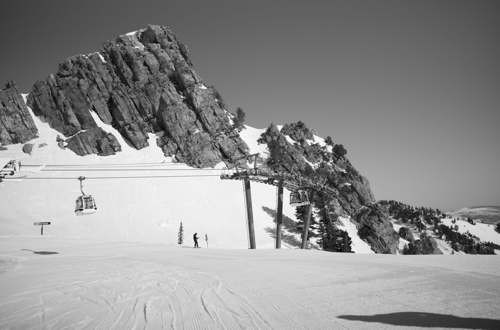 Black and white photo of a snowy alpine slope under a jagged peak, a single skier tiny in the frame.