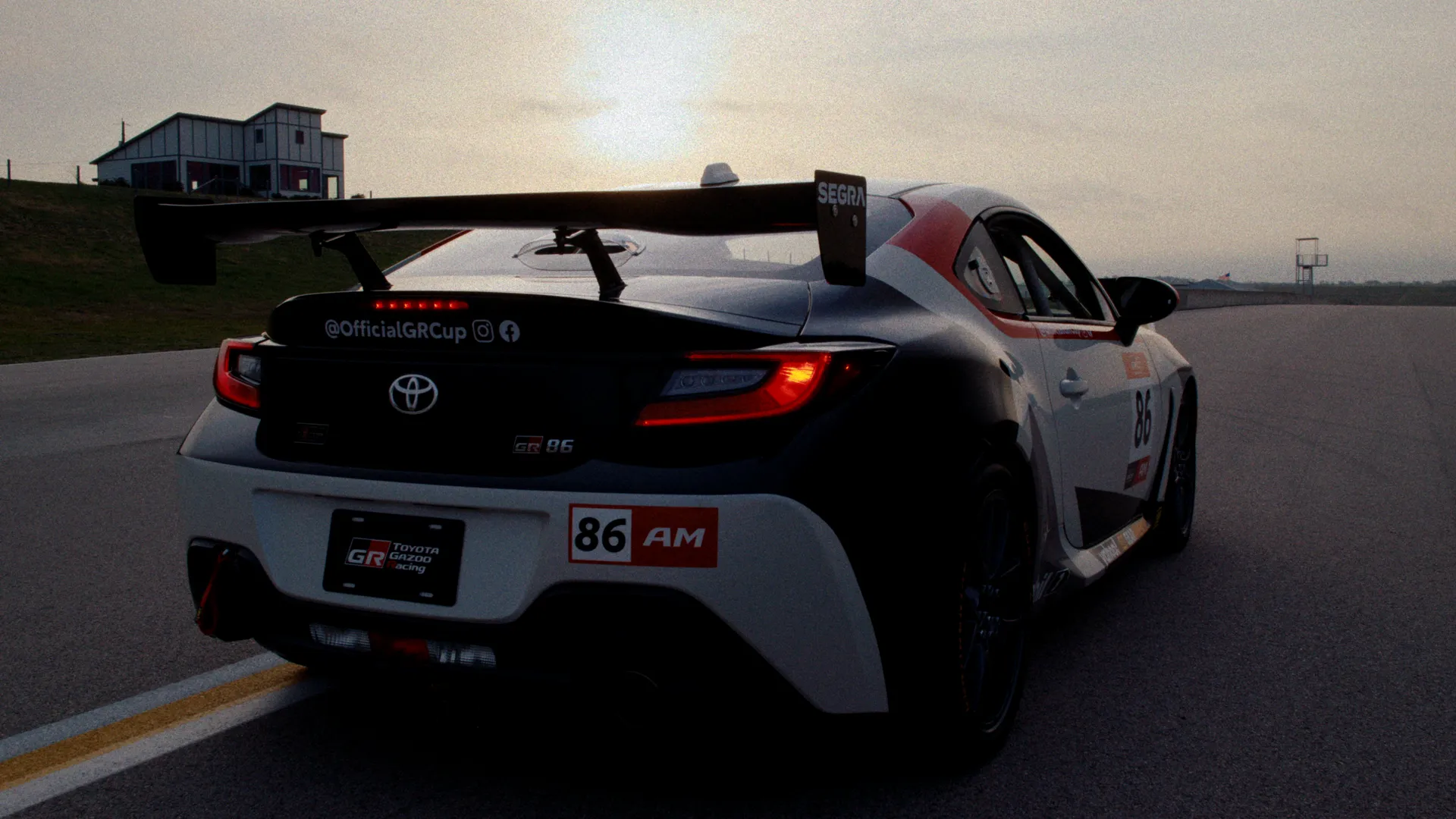Toyota GR86 in GR Cup livery, low rear tracking shot with the sun behind