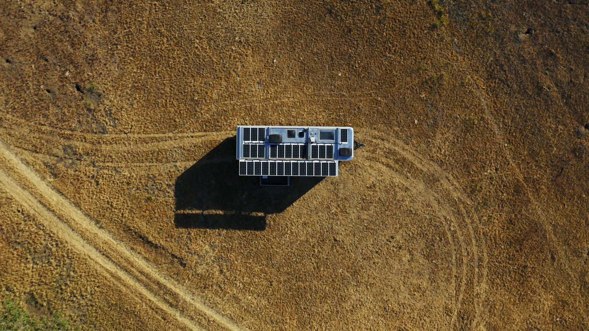 Straight-down aerial on a parked Living Vehicle trailer with looping tire tracks