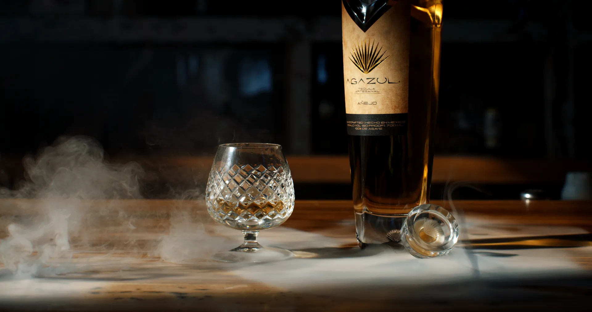 Agazul glass and bottle on a wood bar counter with smoke rising
