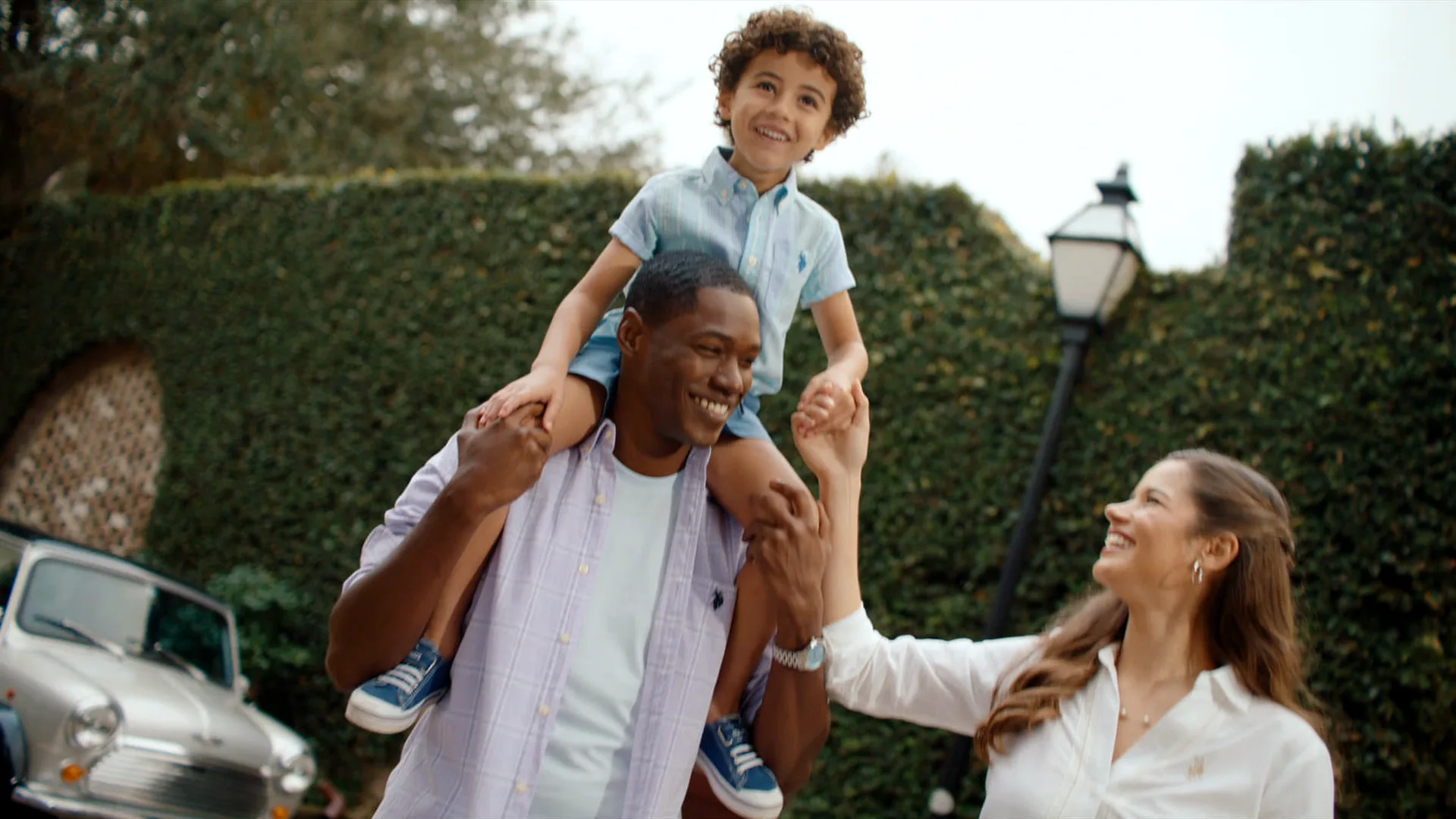 A boy laughing on his dad's shoulders as his mother holds his hand