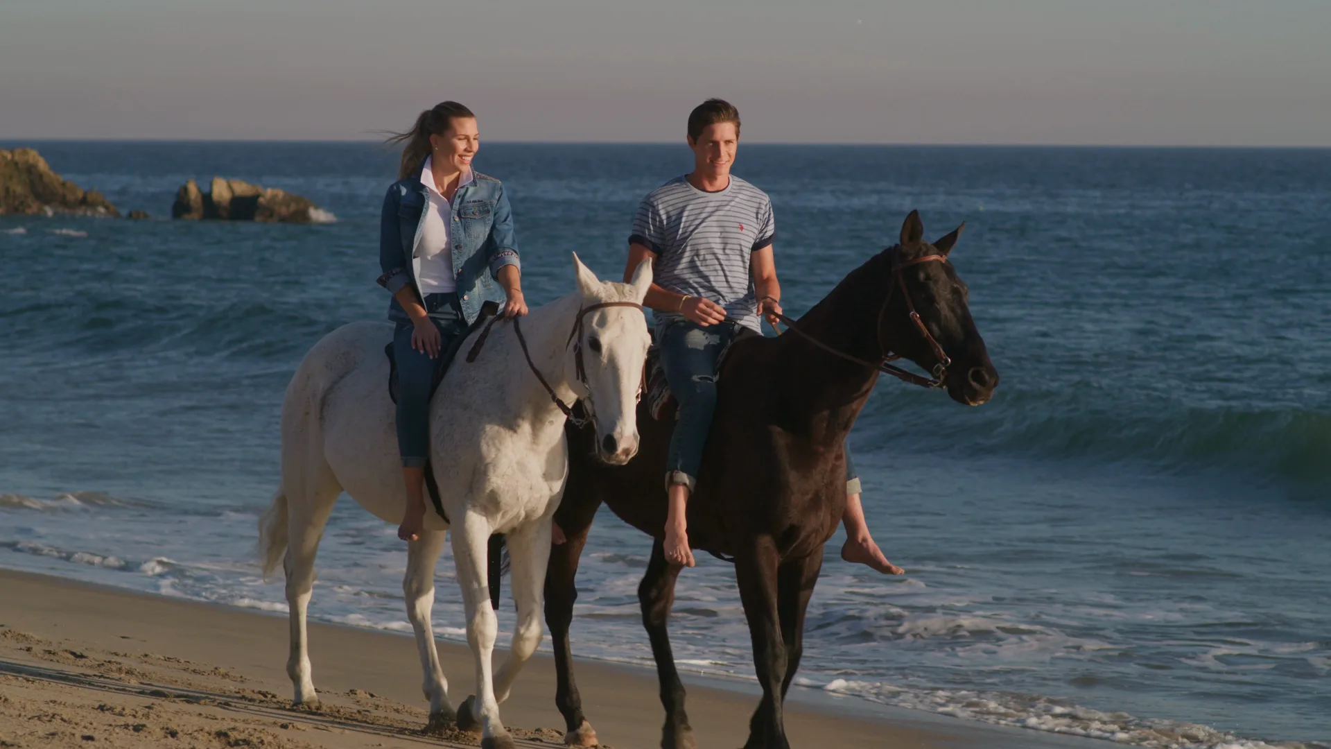 A couple riding horses along the surf at golden hour