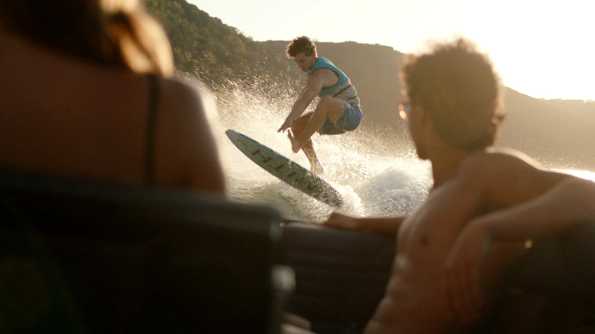 Friends watching a wakesurfer jump in golden light