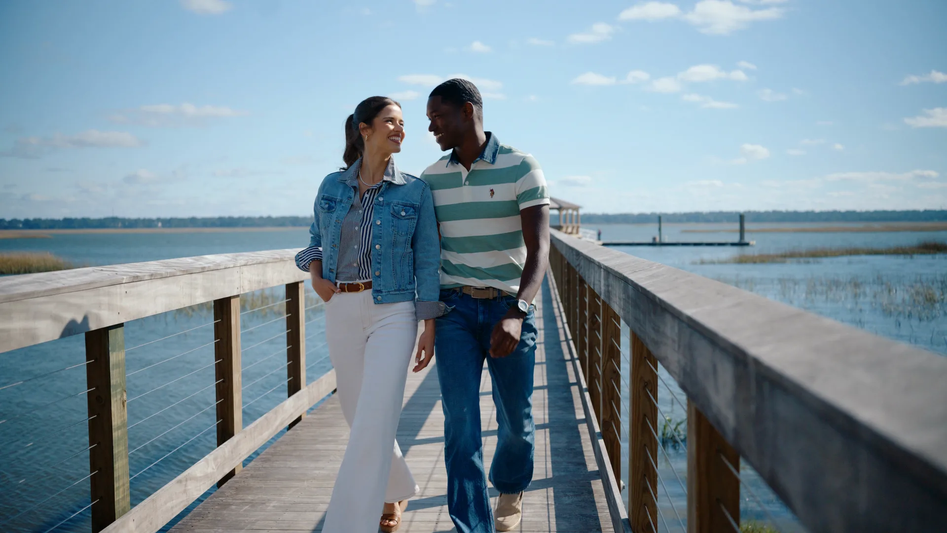 A couple walking a wooden pier over the water, laughing at each other