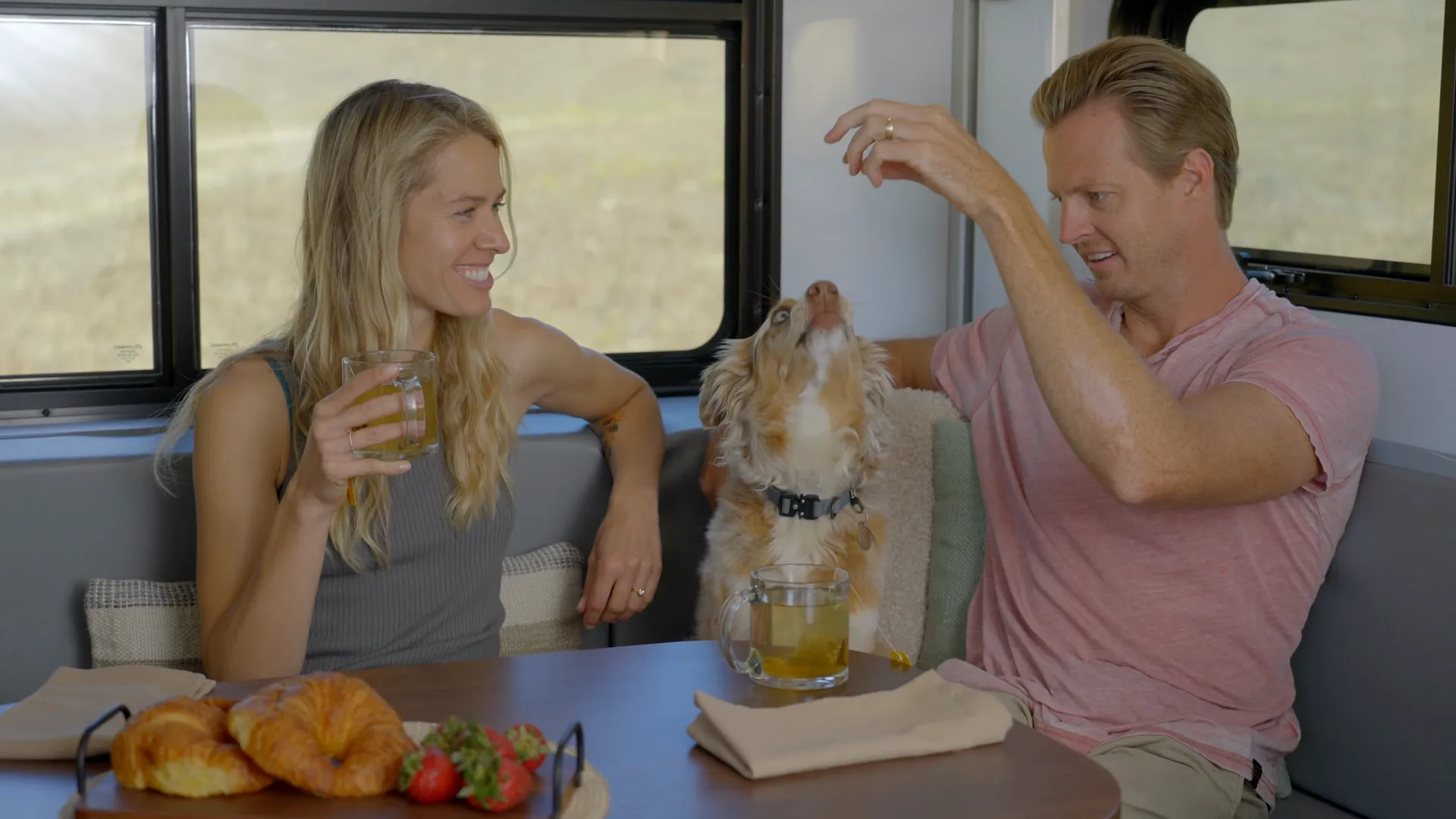A couple at the dinette of a travel trailer as a dog licks the man's hand