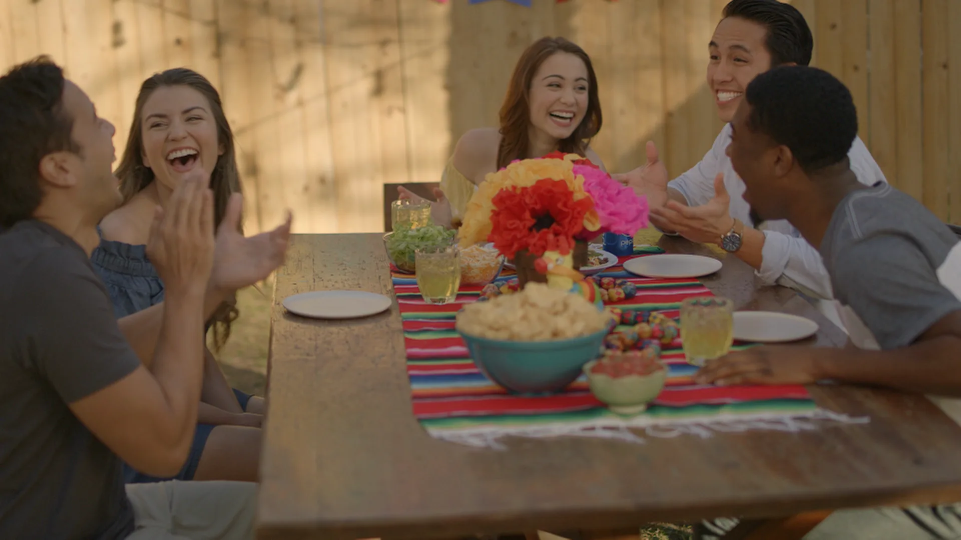 Friends laughing around a backyard table under a striped tablecloth