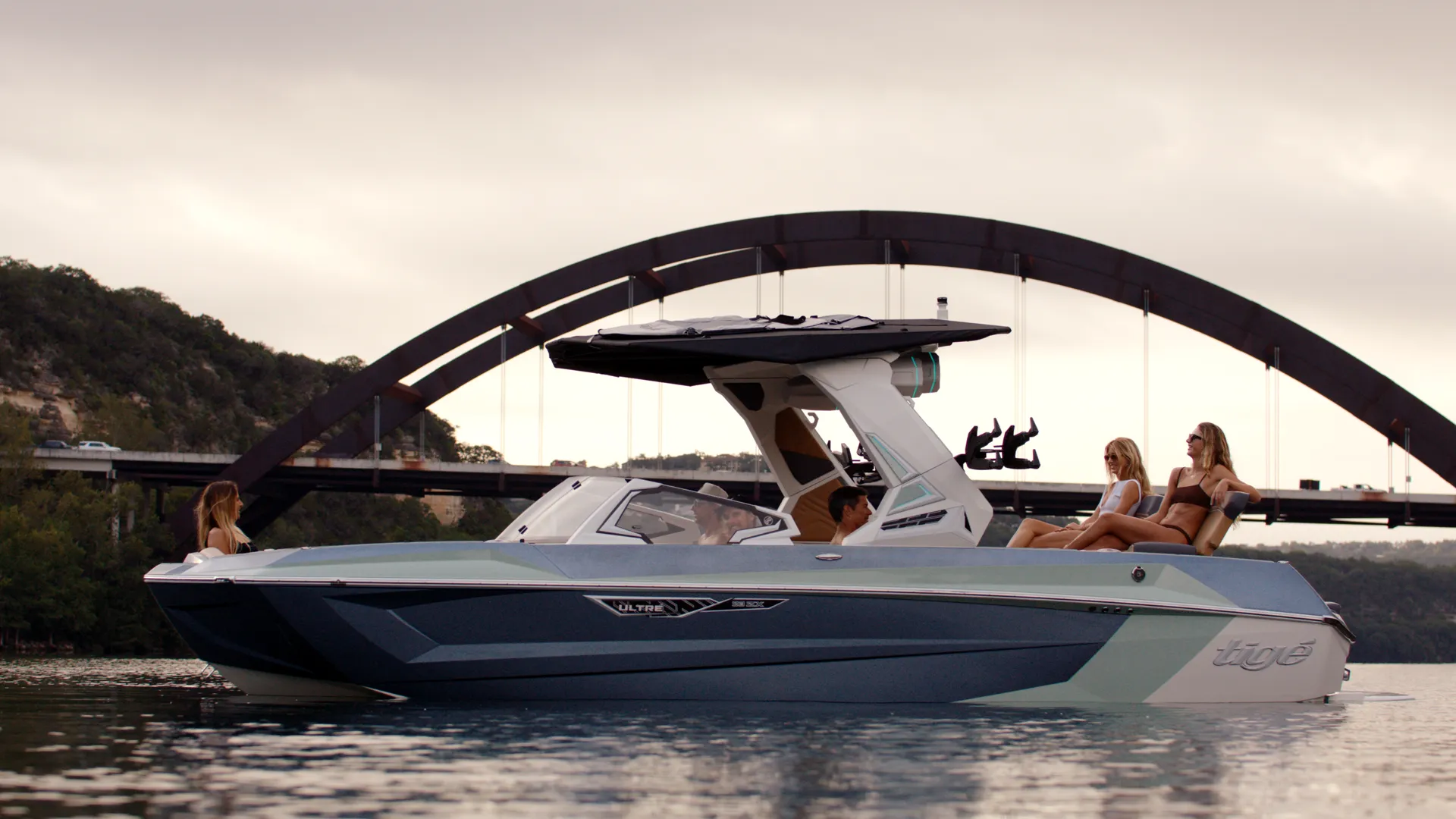 Tige boat passing under Austin's Pennybacker Bridge arch with riders lounging