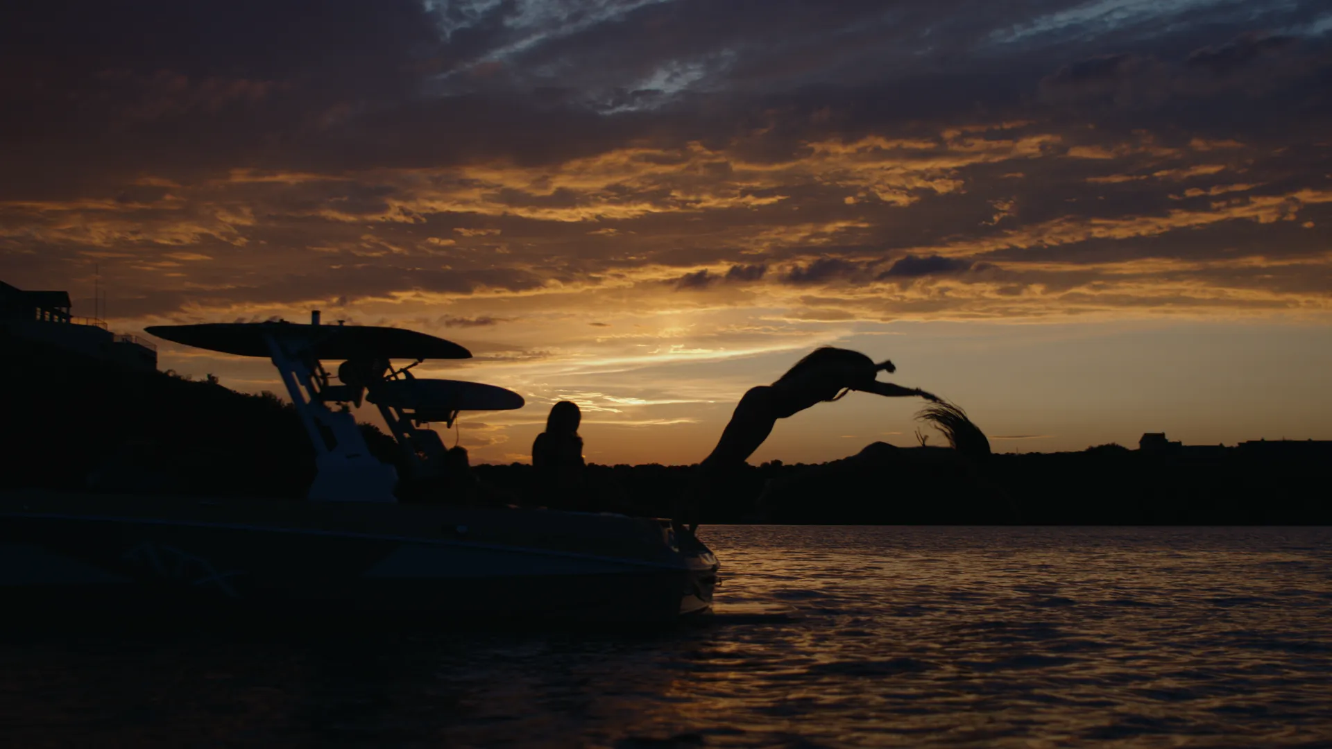Boat silhouette against an orange sunset as a rider dives from the tower