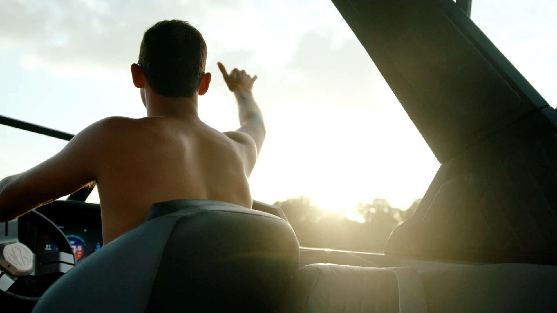 Driver at the helm points ahead, backlit by the low sun