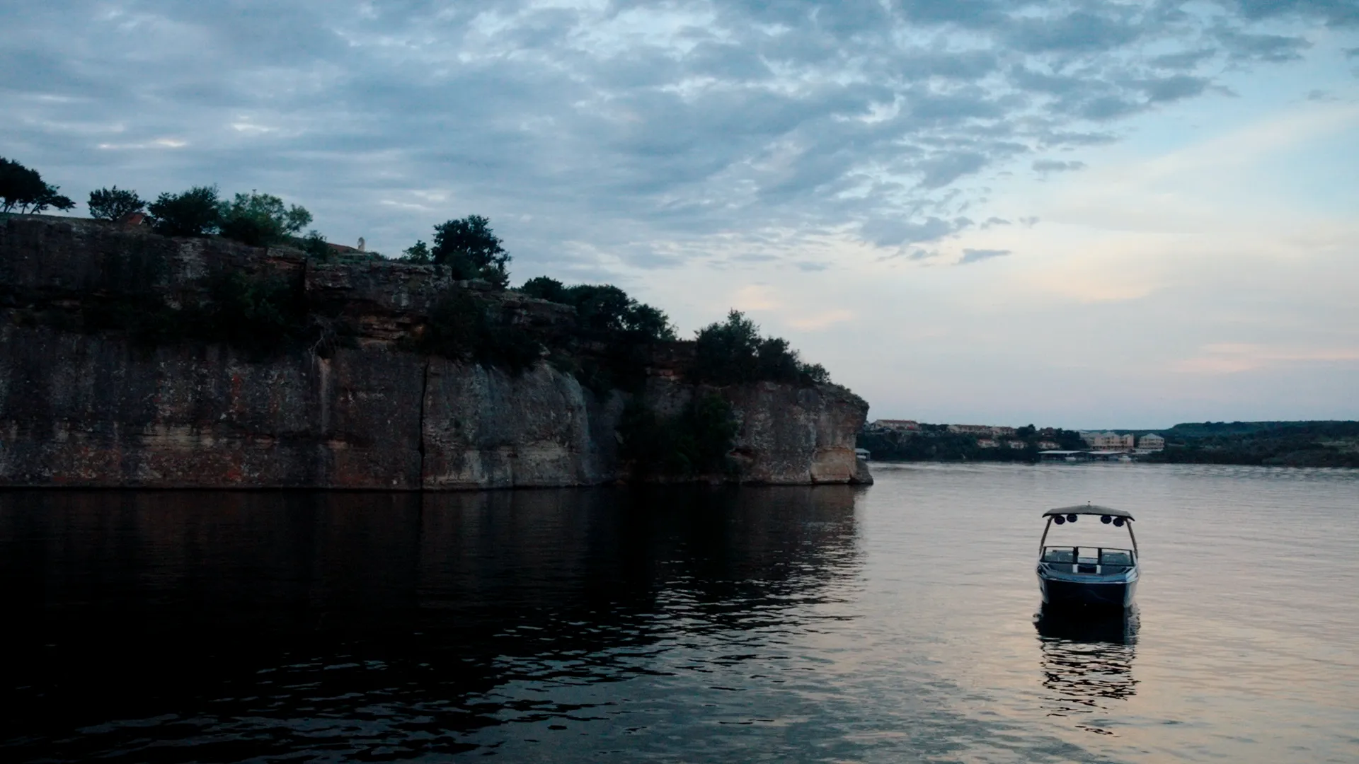 Tige boat idling beneath limestone cliffs on still water