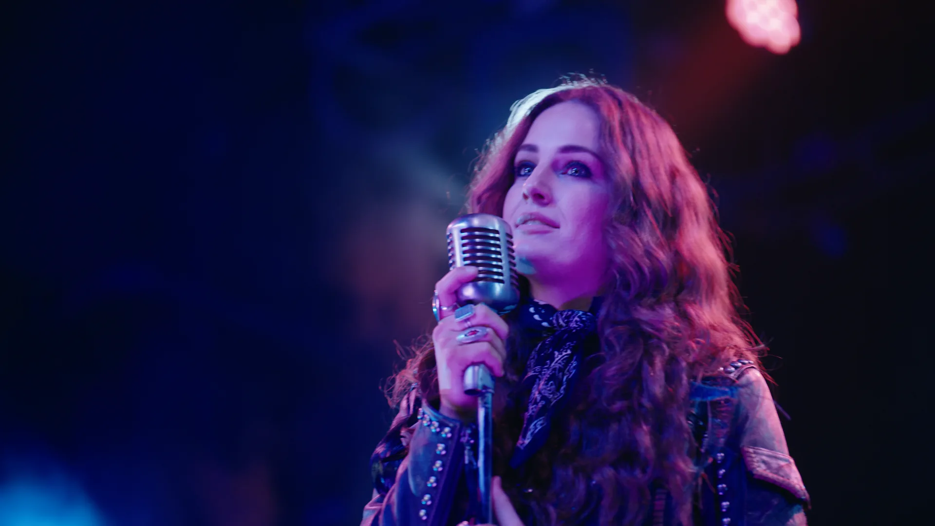 Kat Hasty singing into a vintage mic under red and blue stage light
