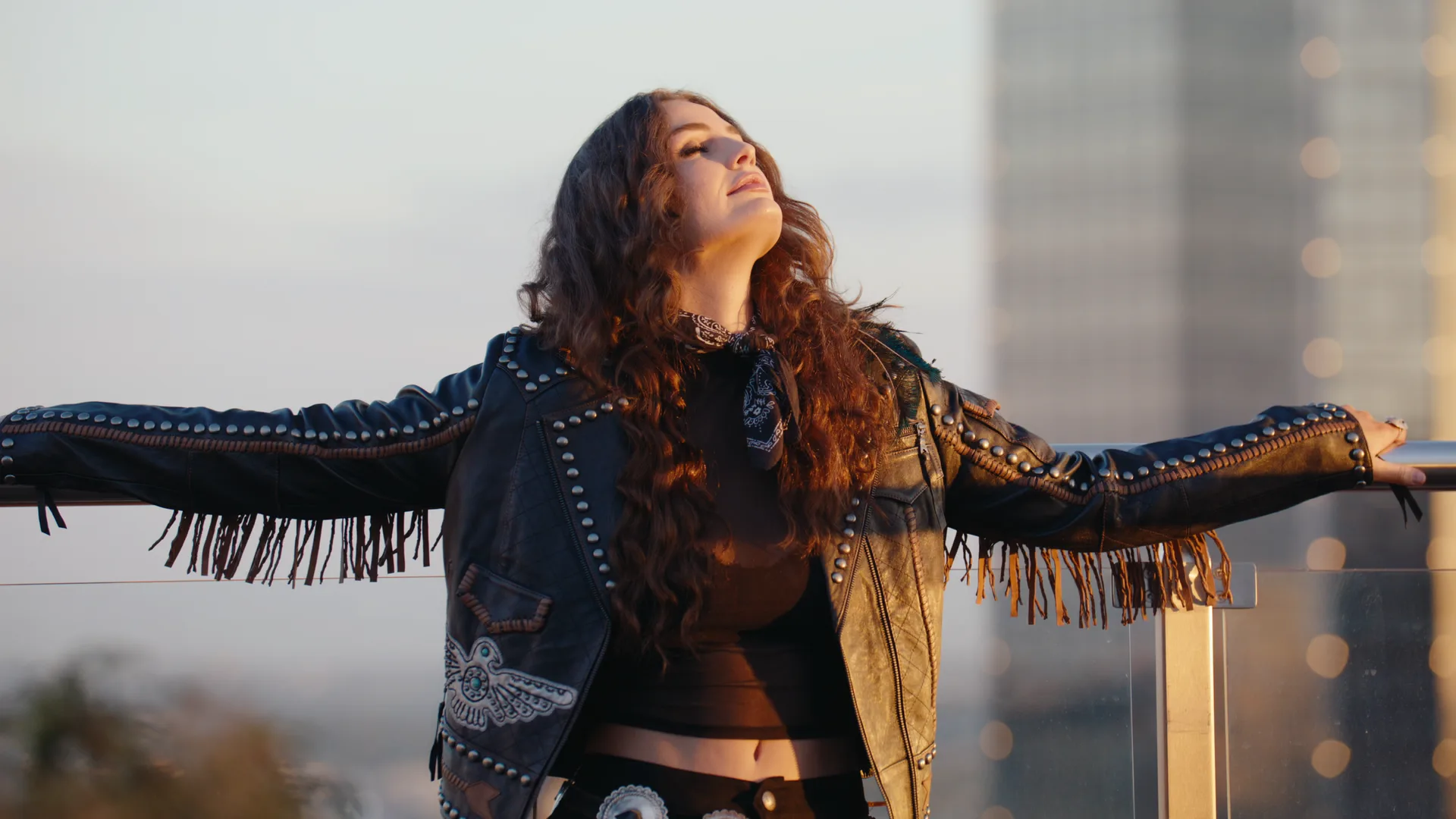 Kat Hasty with arms out on a rooftop rail at golden hour