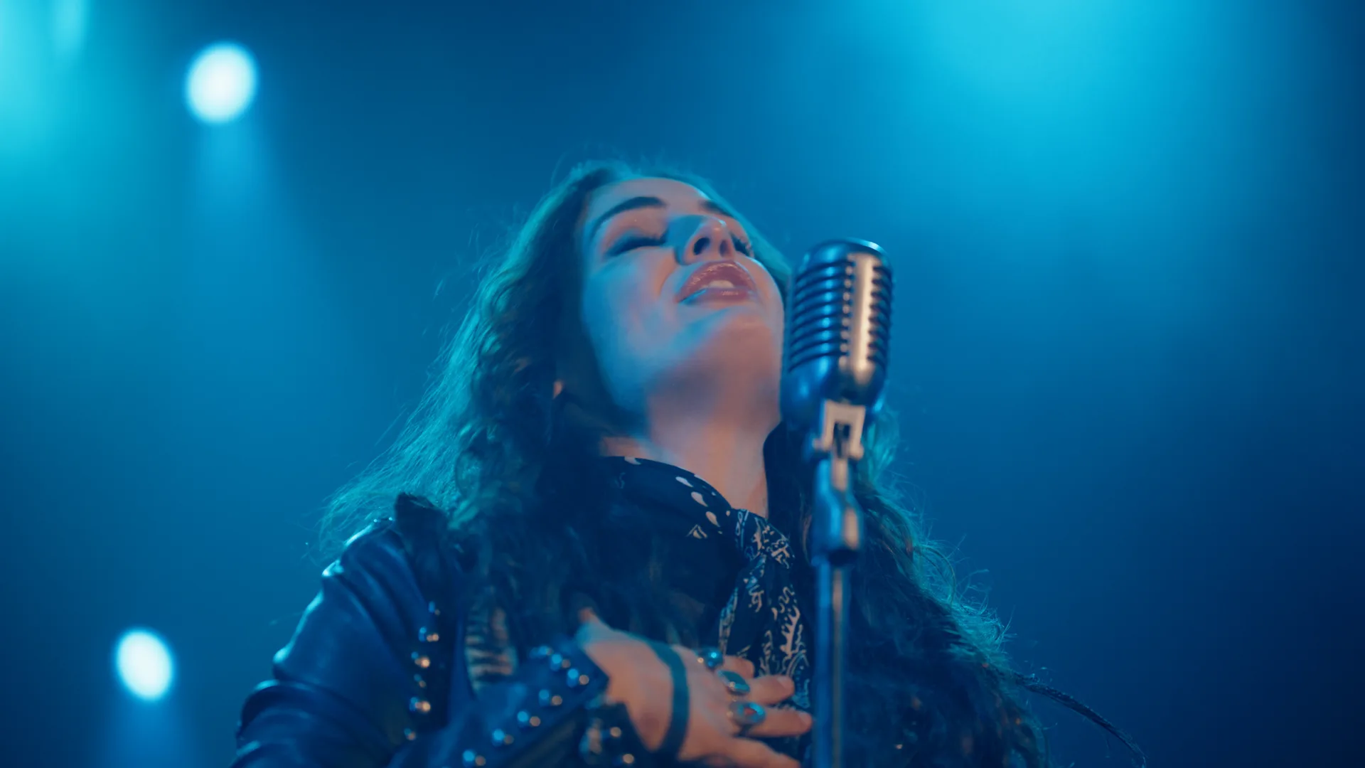 Kat Hasty singing with eyes closed in blue stage haze