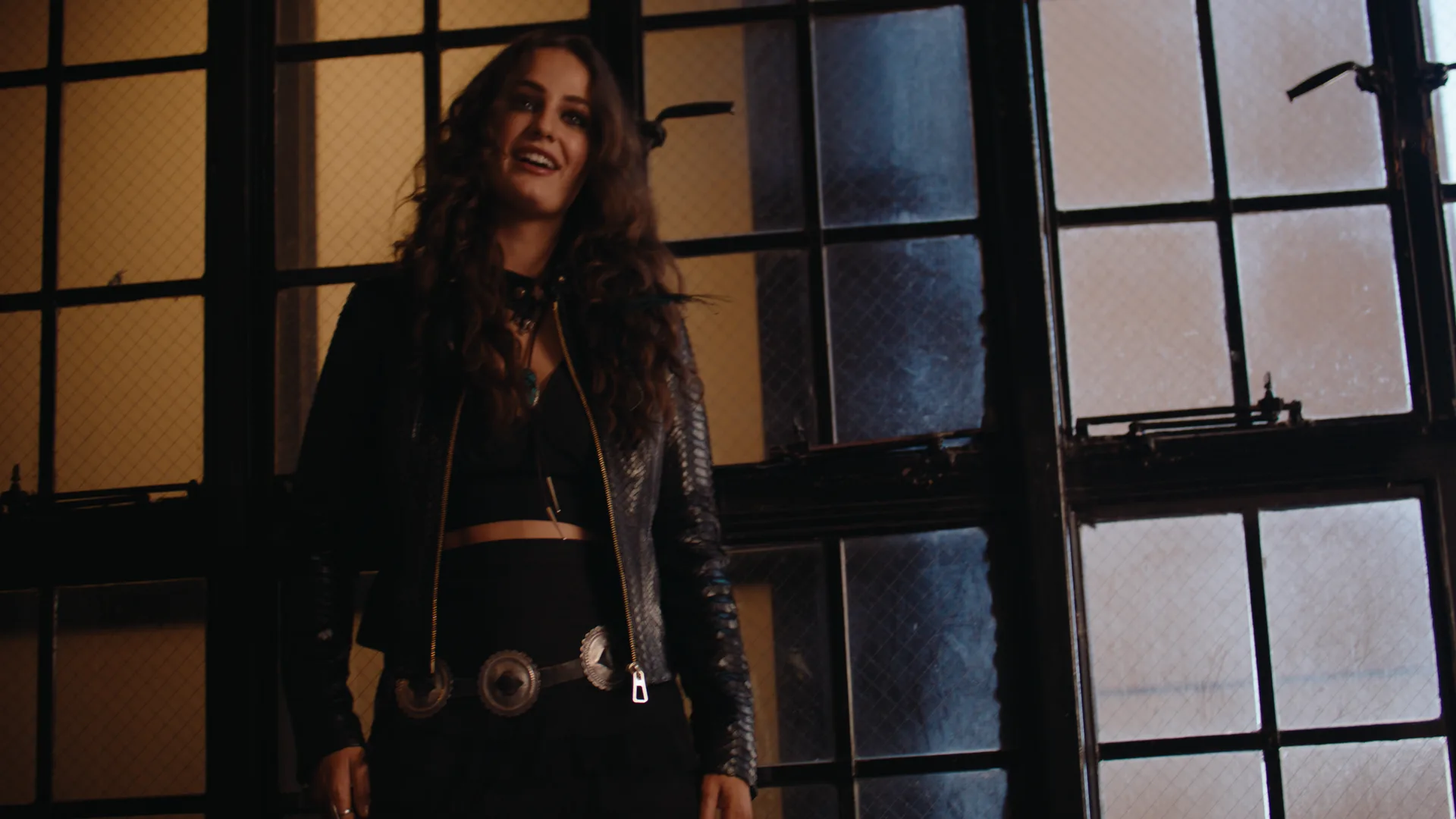 Kat Hasty in a leather jacket against tall factory windows