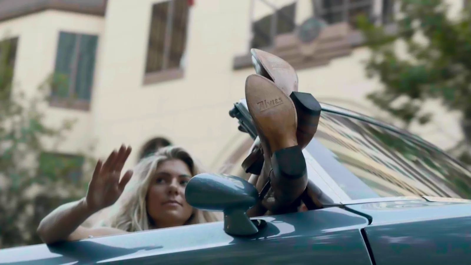 Passenger waving from a convertible with her boots up on the door