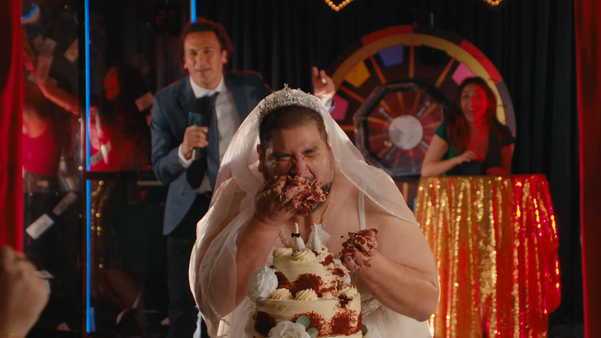 A game-show host with a microphone beside the cake-covered man in a wedding dress
