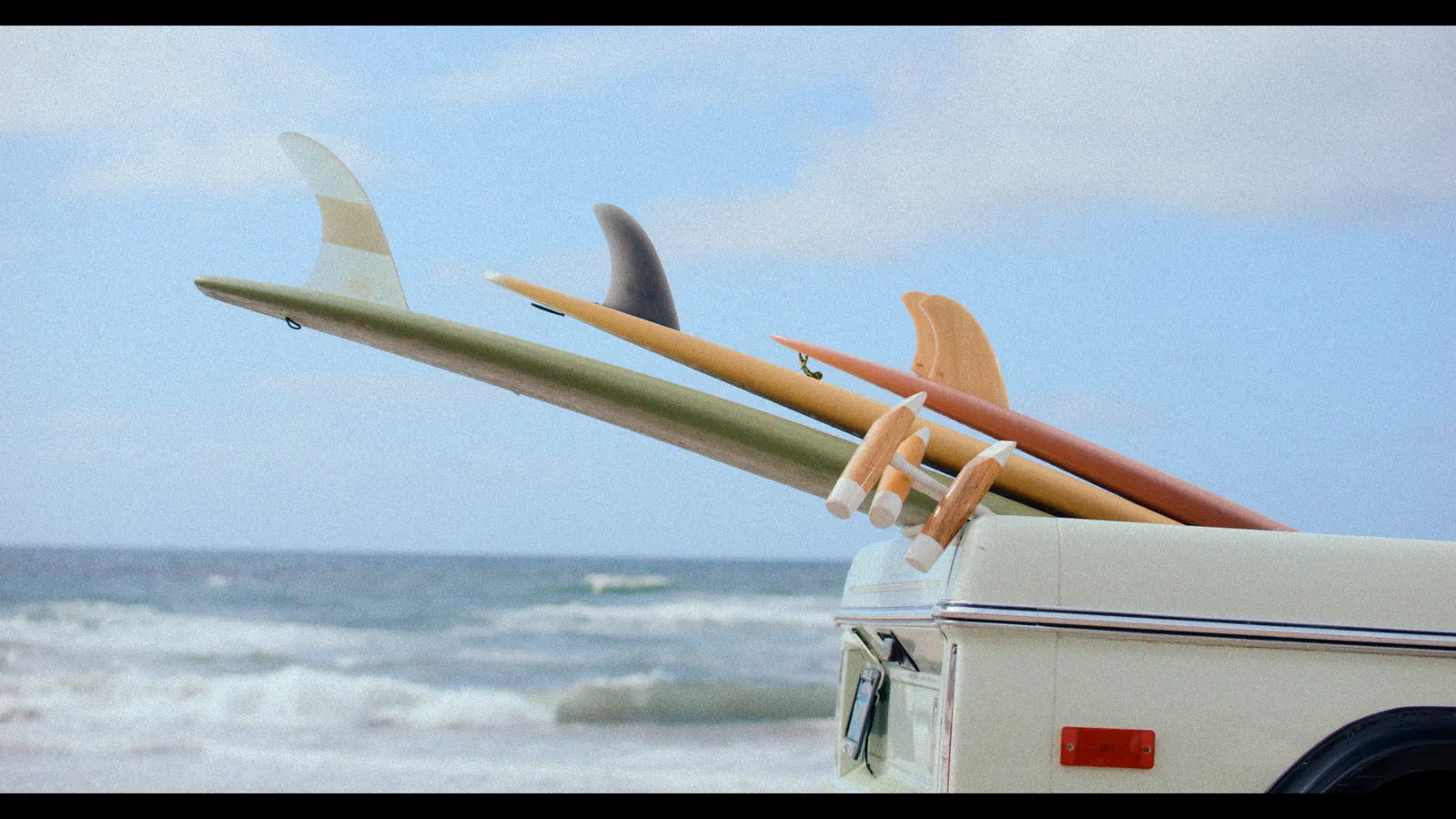 Surfboards strapped to a vintage Bronco above the surf