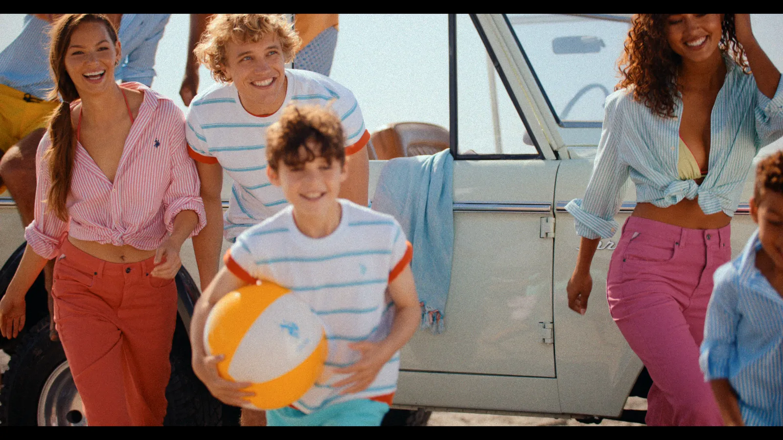 Friends with a beach ball running past a vintage Bronco