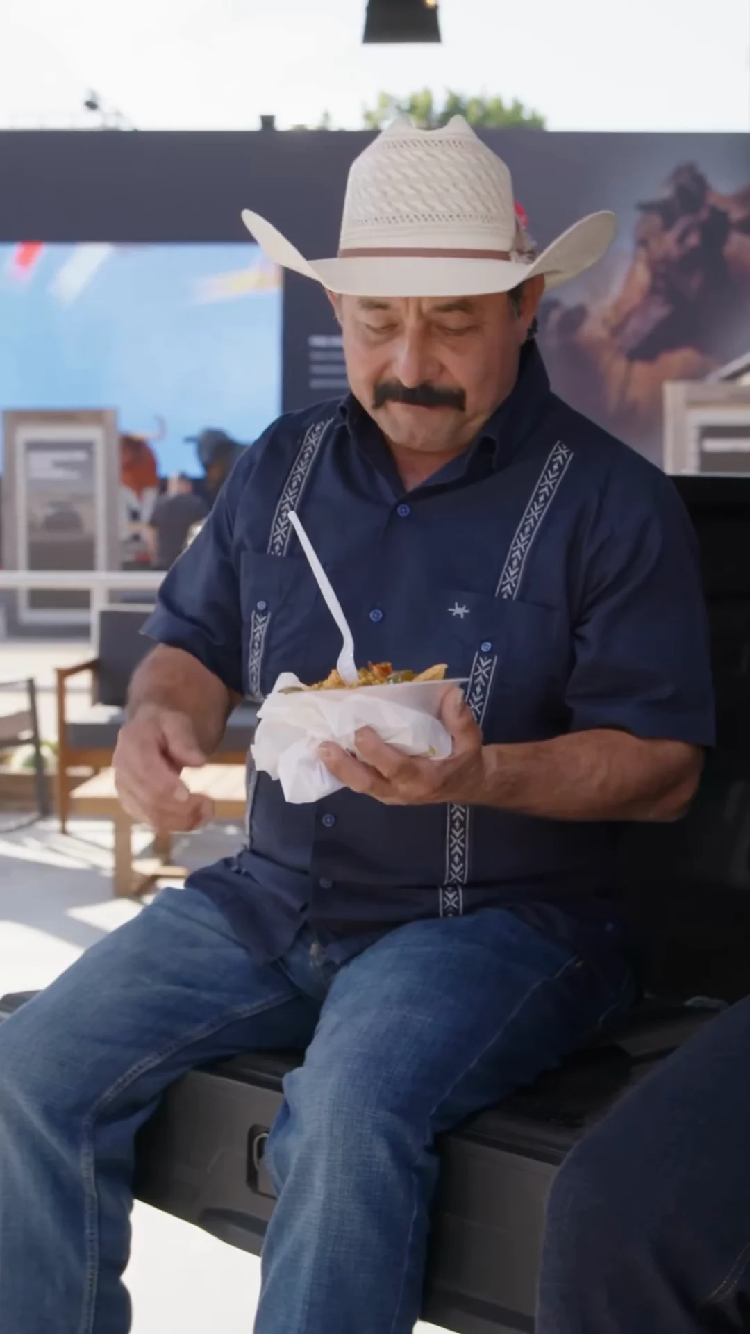 A reviewer in a straw hat digging into a Frito pie on the tailgate