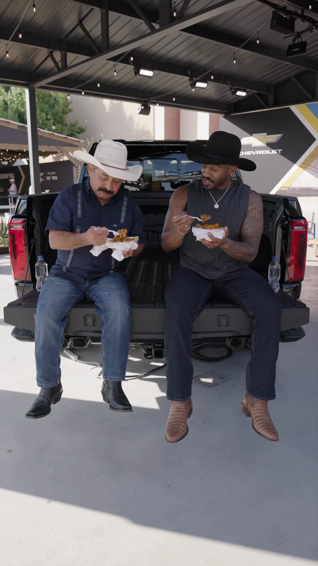 Both reviewers eating on the tailgate of a Silverado under the pavilion