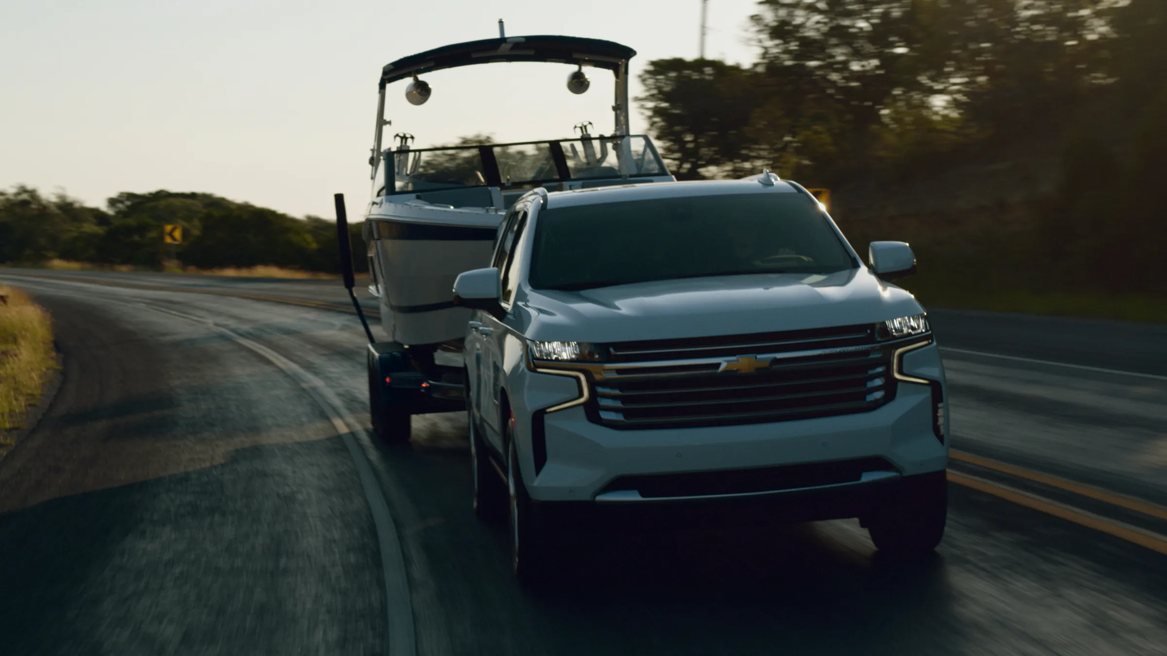 The Suburban towing the Cobalt around a curve on a Hill Country road, backlit by low sun on the asphalt