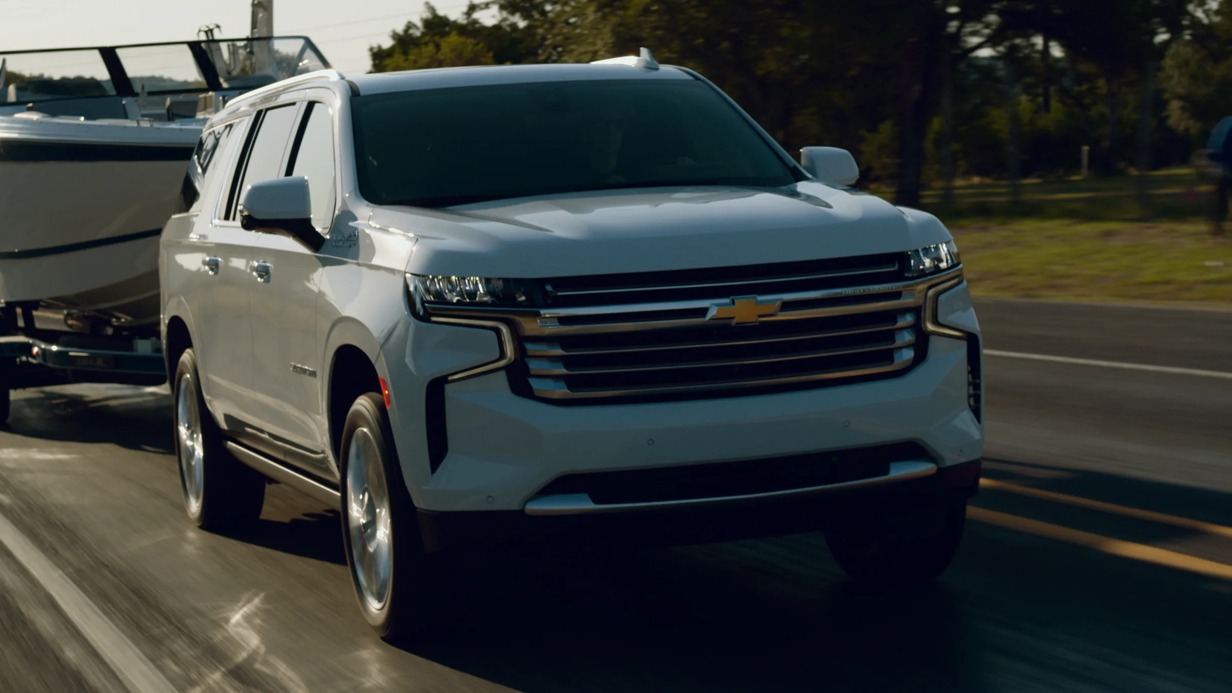Close three-quarter view of the Suburban's grille at speed, the boat glowing behind it
