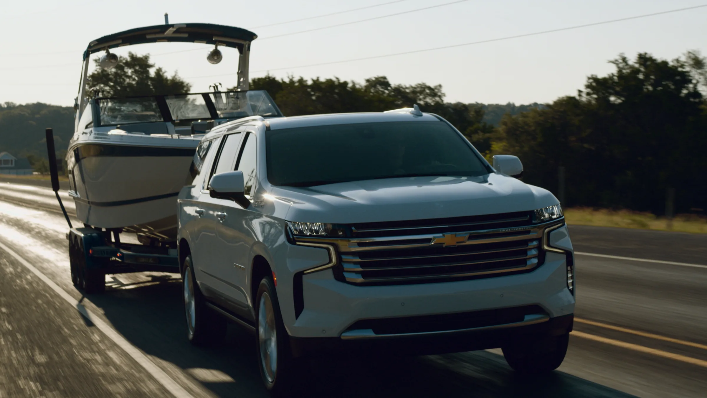 Low, close tracking shot of the Suburban on a sunlit road that sparkles at sunset