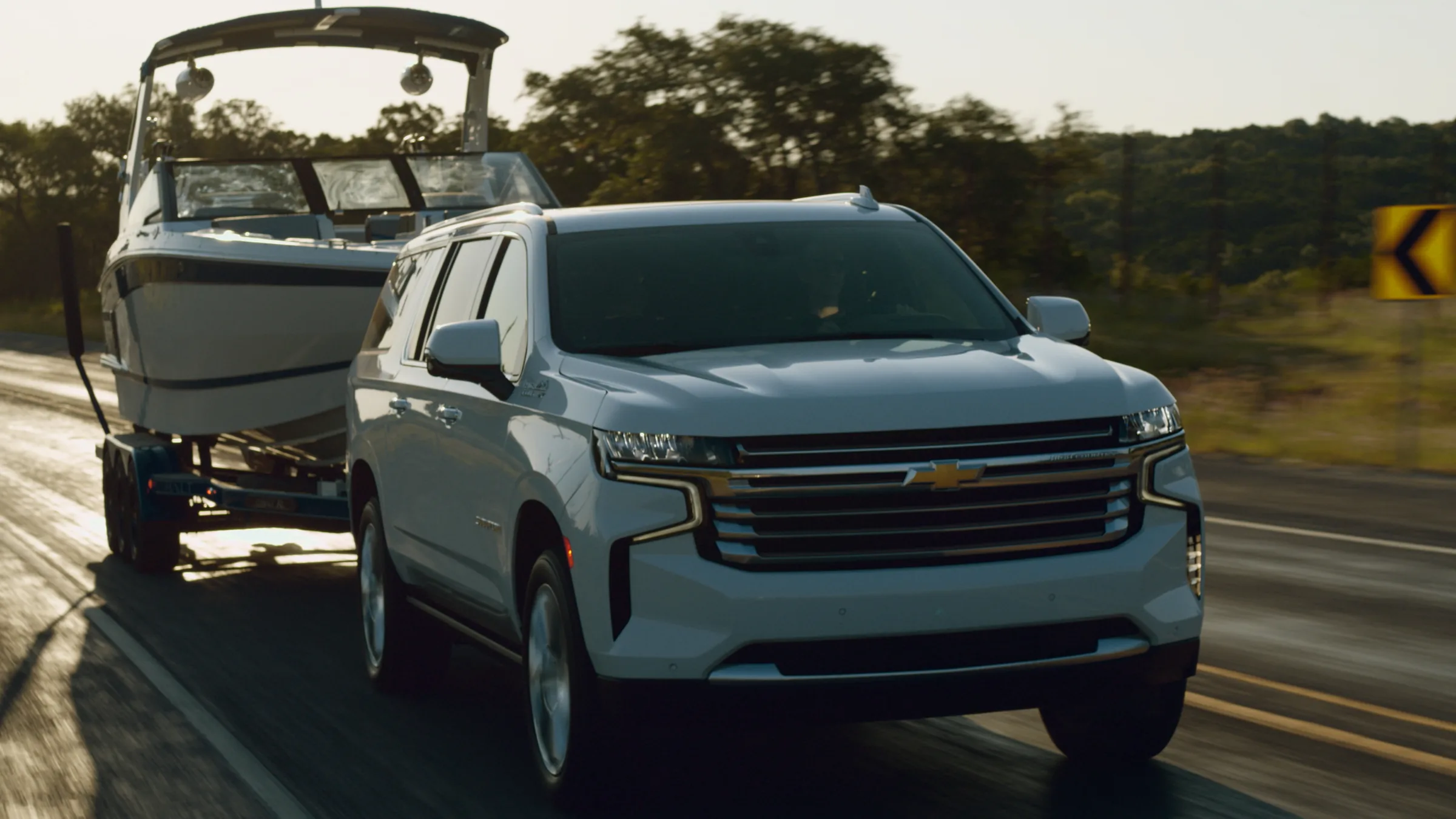 Low angle on the Suburban and boat on a wet road, rim lit by the setting sun