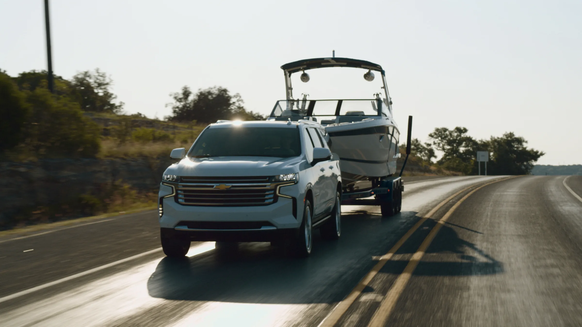 The Suburban and boat on a backlit road with sun glare on the asphalt
