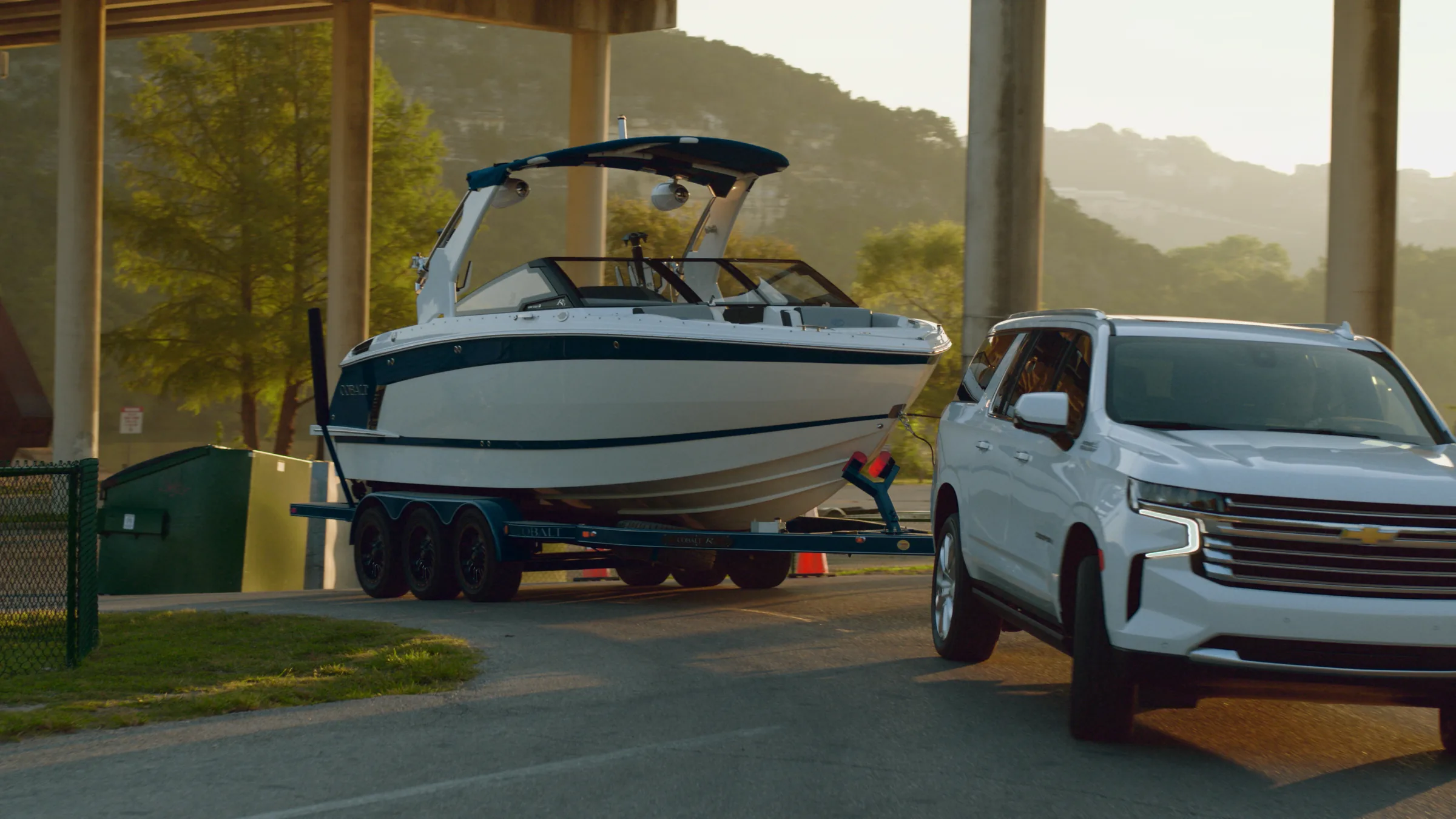 The Cobalt in profile under the bridge in golden light, the Suburban beside it