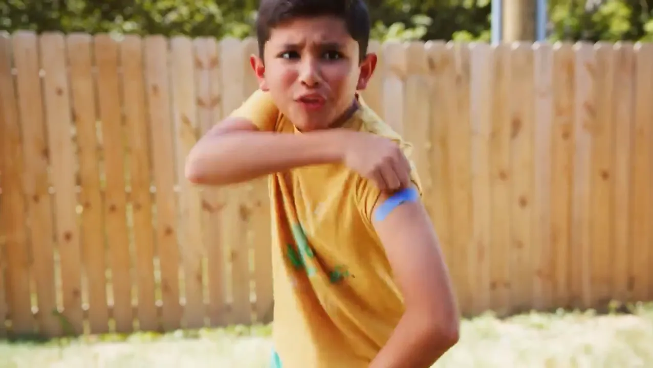 A boy in a yellow shirt showing off the bandage on his arm
