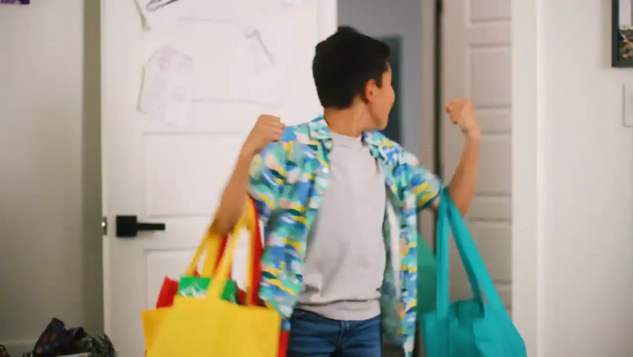 A boy carrying bright shopping bags toward the door