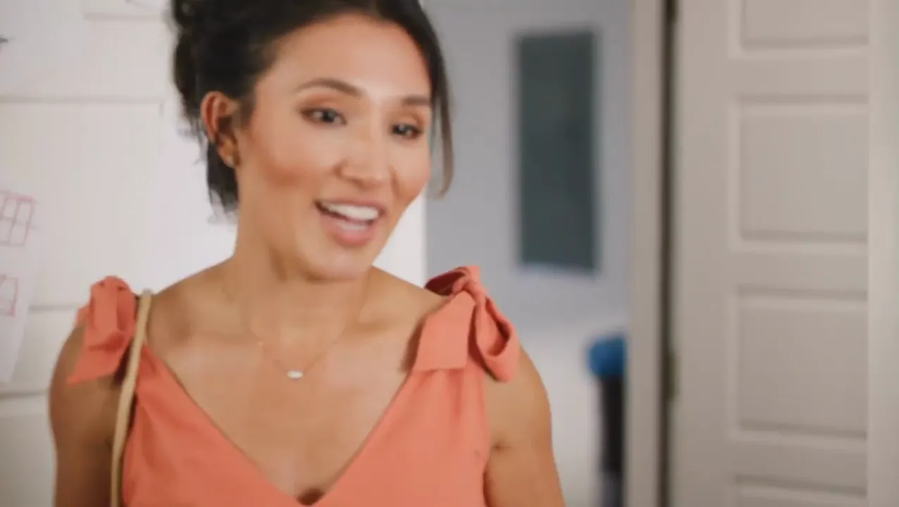 A woman smiling as she talks to camera in a hallway