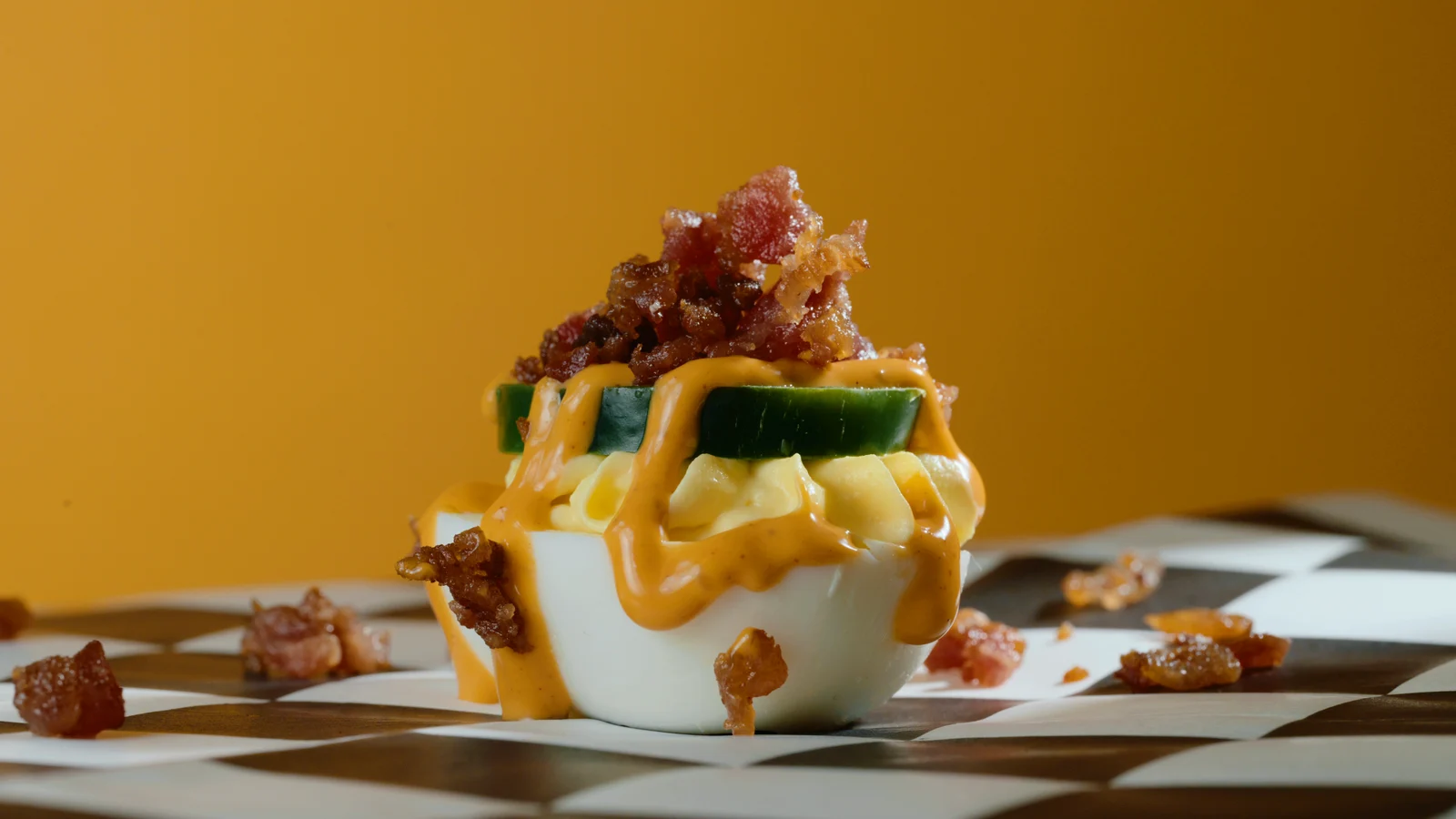 Bacon mustard deviled egg on a checkerboard set against a gold sweep
