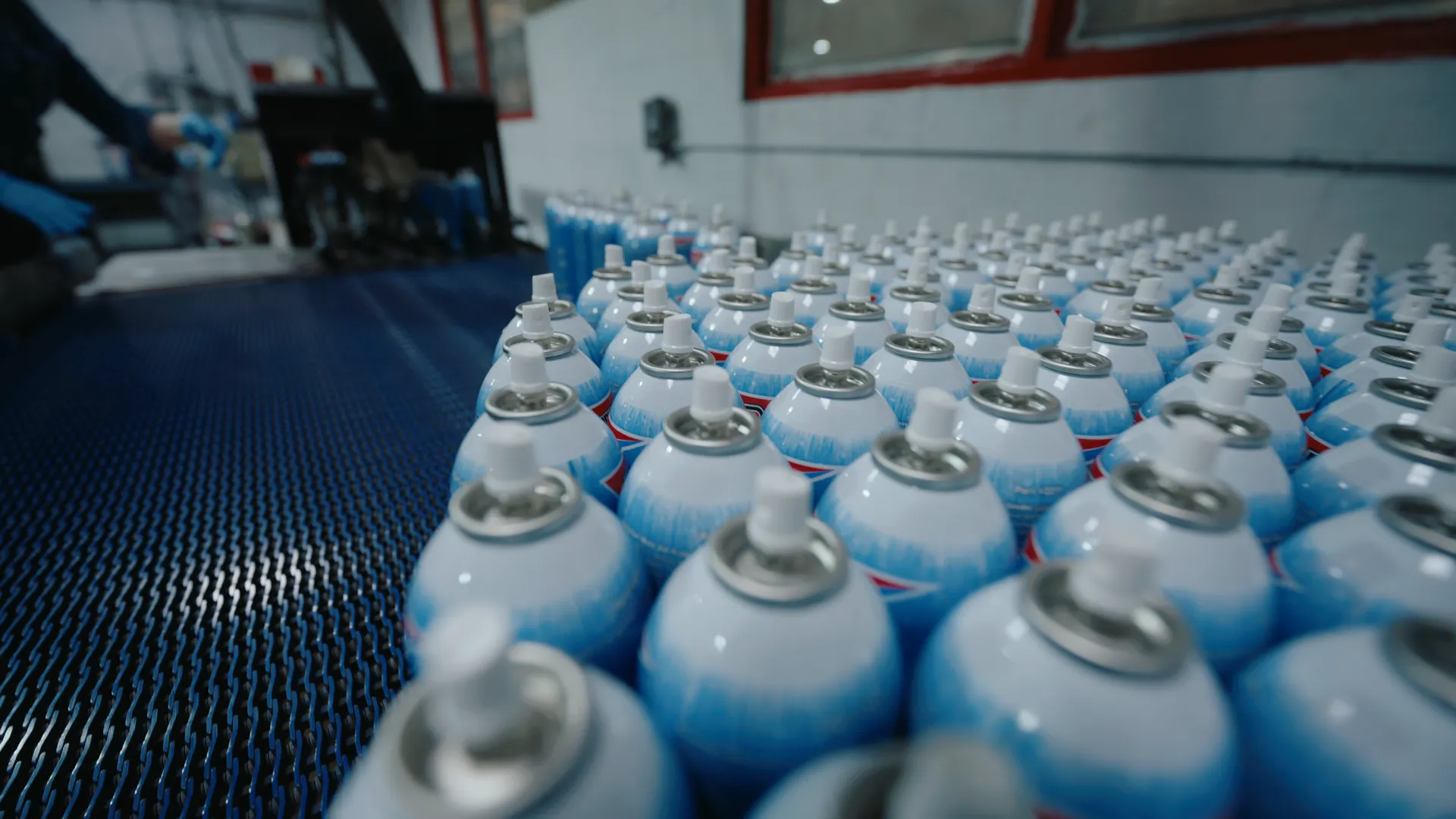Rows of spray cans queued on a blue production conveyor, shallow focus