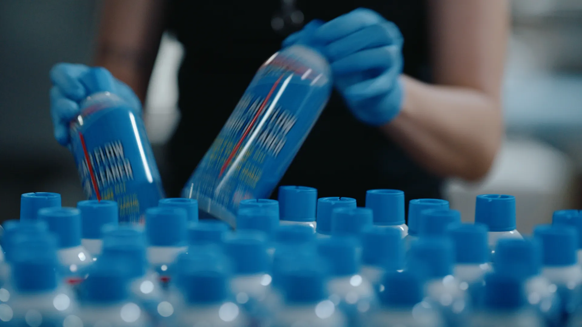 Gloved hands working a row of products topped with blue caps