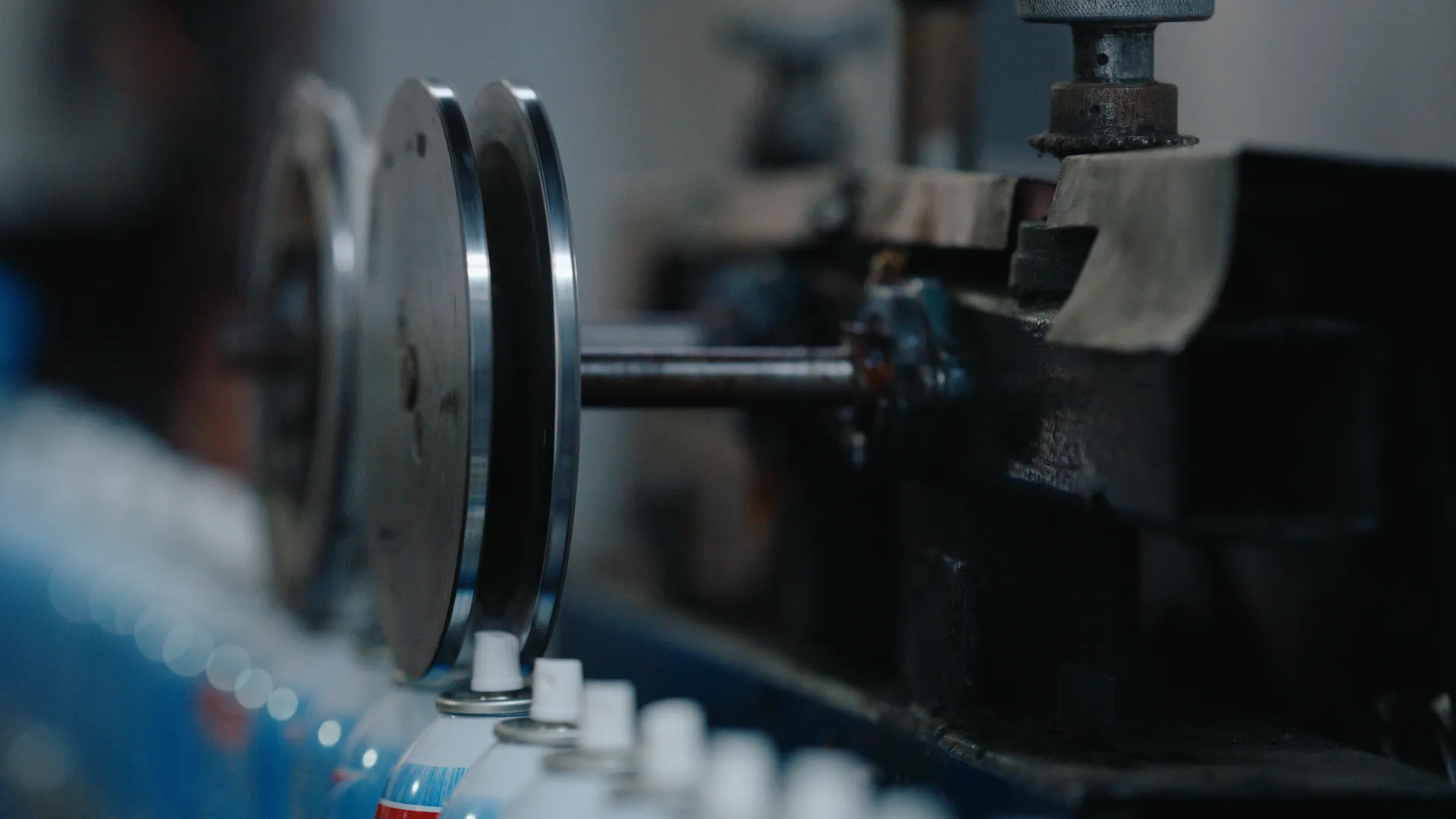 A steel guide wheel turning above a row of blue aerosol cans