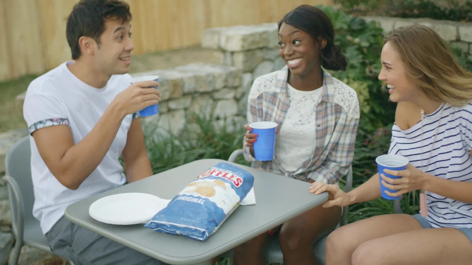 Friends at a patio table with a bag of Lay's and blue cups