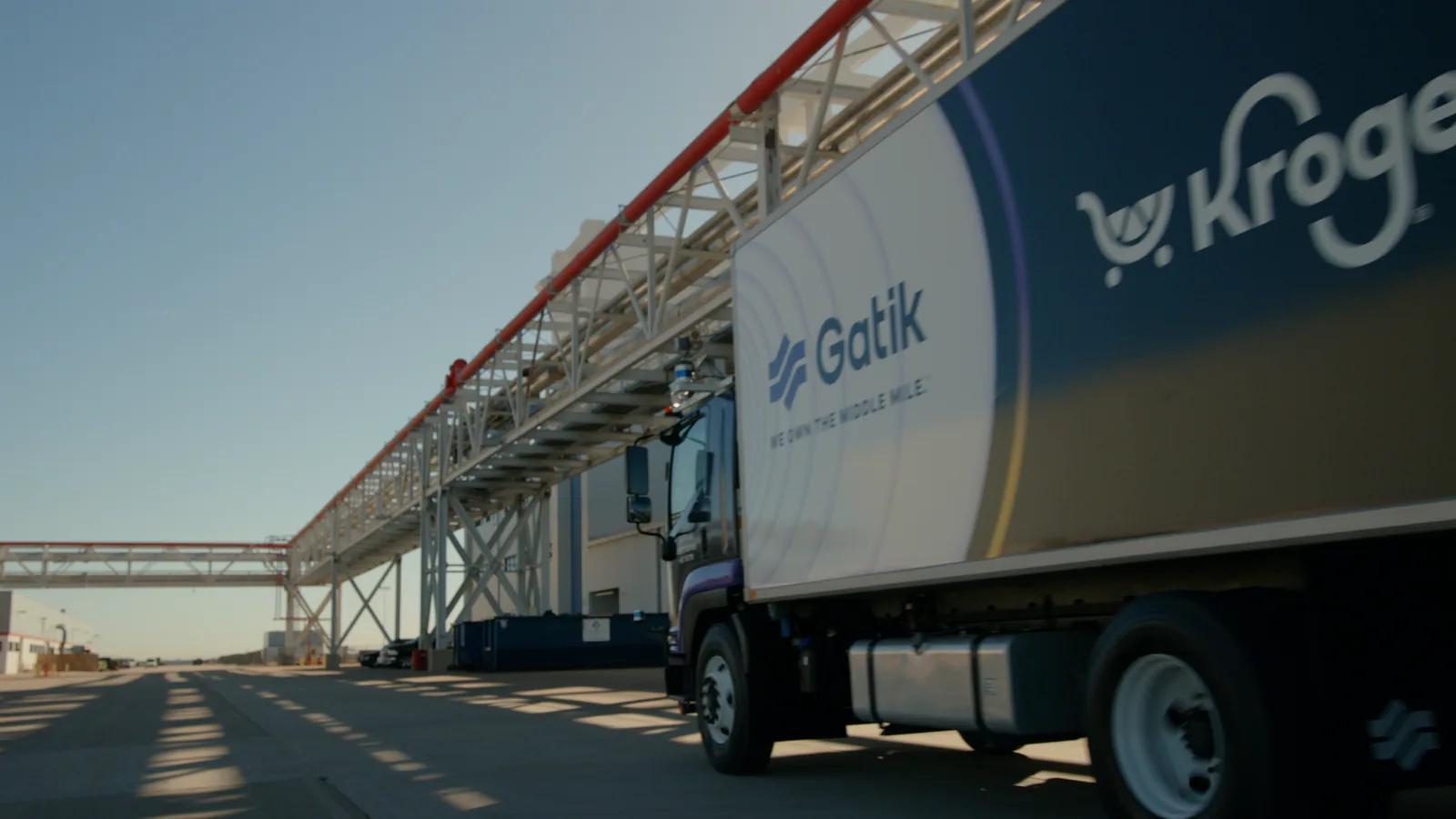 Low wide pass along an airport hangar as a Gatik box truck slides through frame