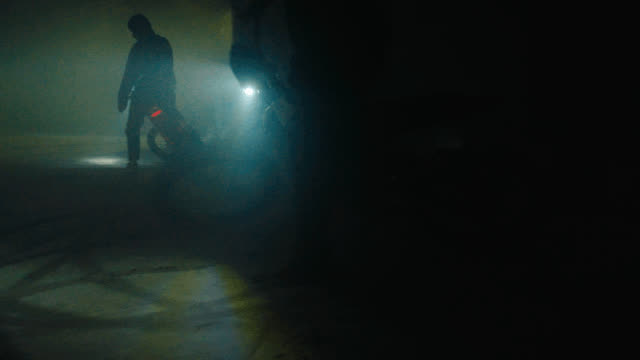 A rider with a headlight emerging from fog inside a warehouse