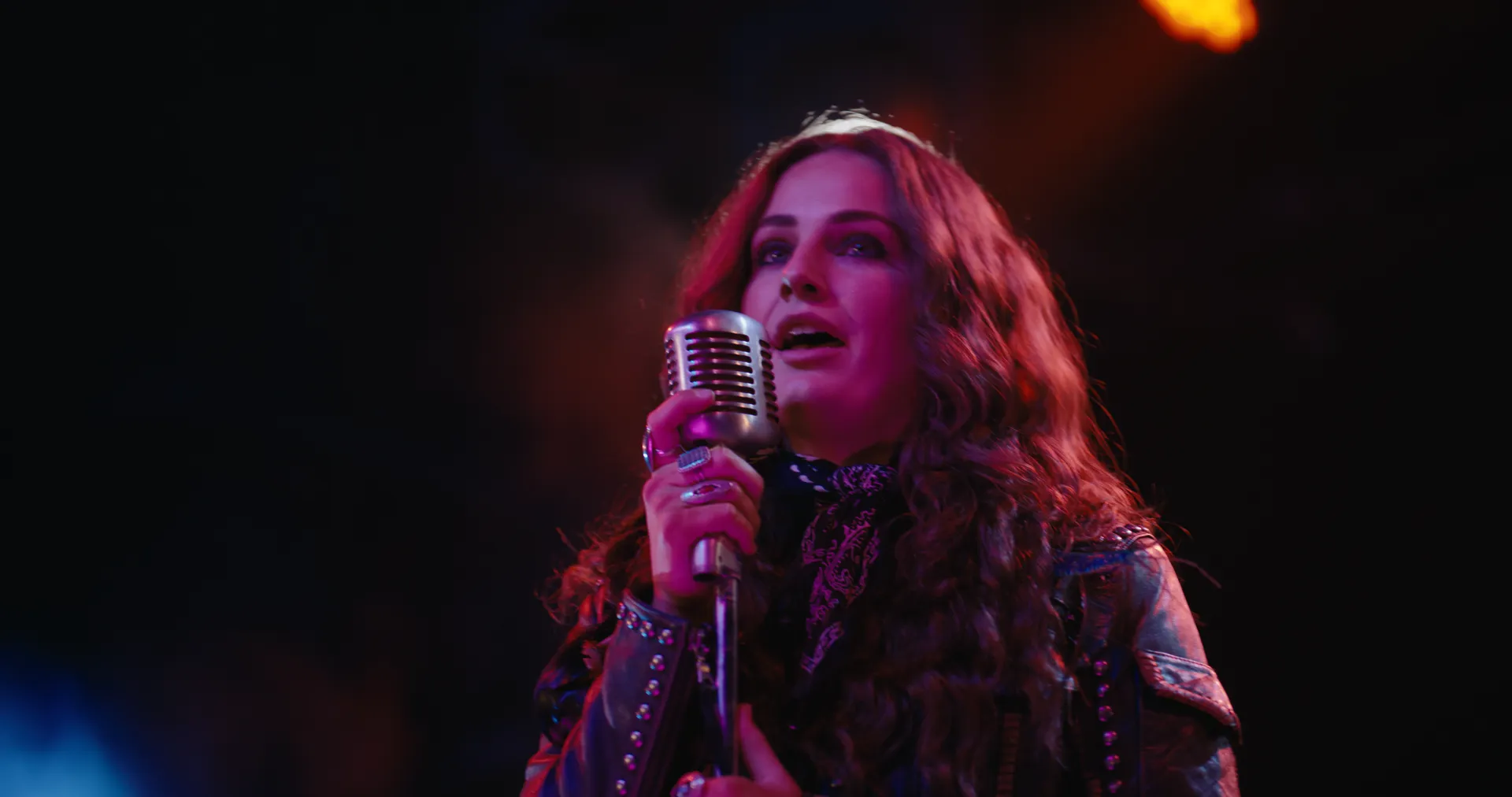 Khasty singing into a vintage microphone under red stage light