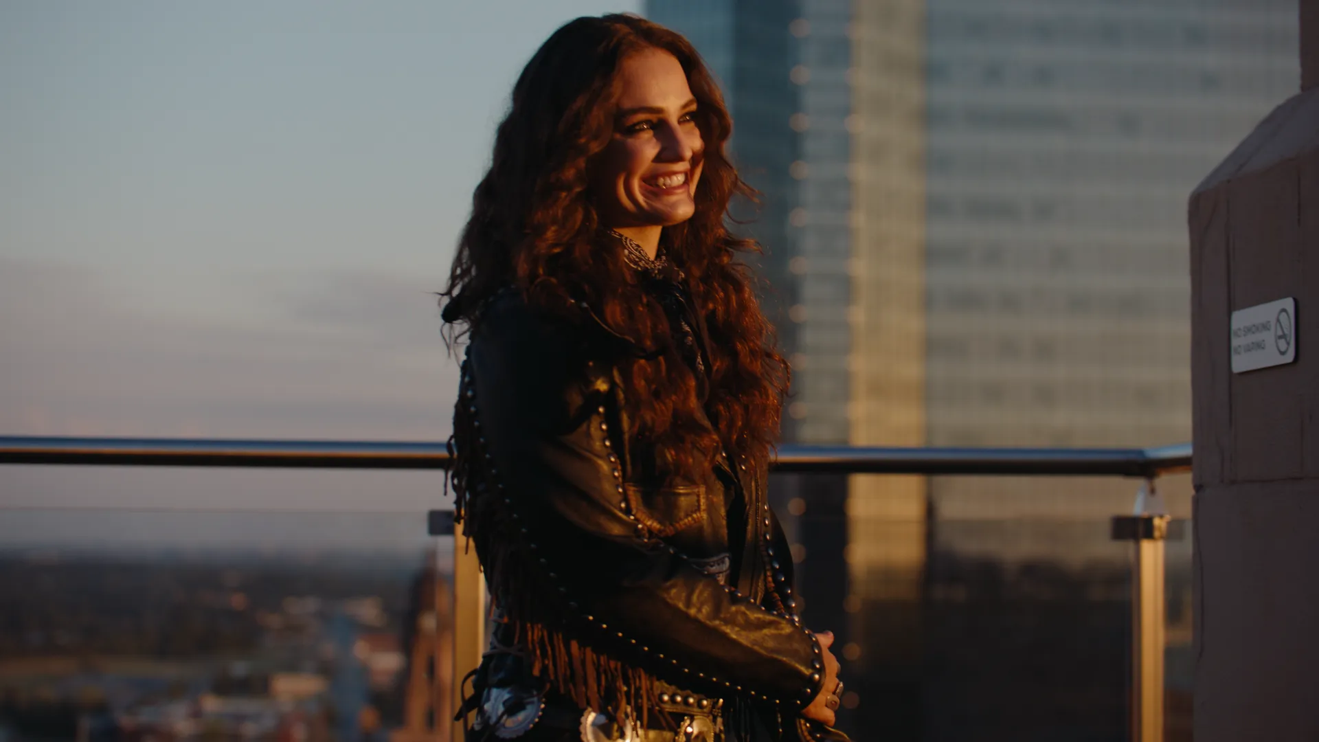 Khasty smiling at the rooftop rail with the skyline behind