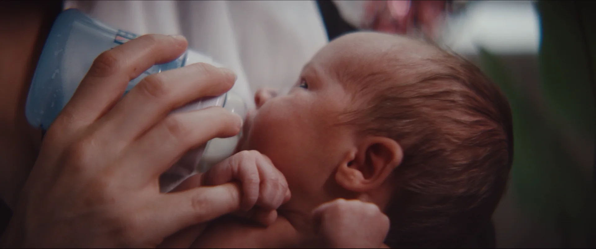 A mother bottle-feeding her newborn, a tiny hand wrapped around the bottle