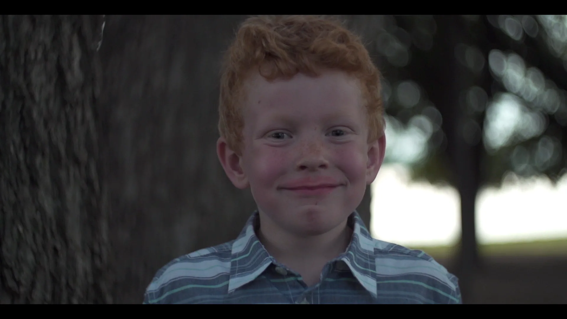 A red-haired boy grinning at a lakeside family cookout