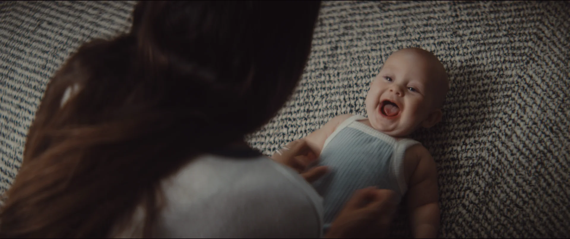 A baby laughing on a rug as her mother leans over her