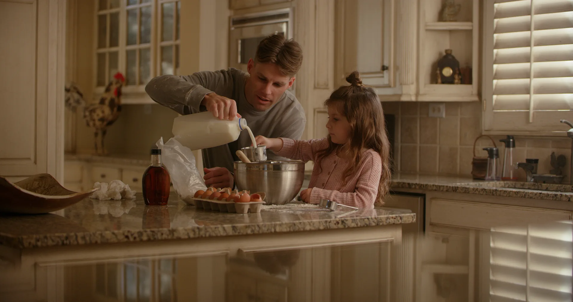 A father pouring milk into a mixing bowl while his daughter stirs